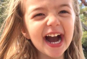 A close up headshot of a cute little girl laughing outdoors