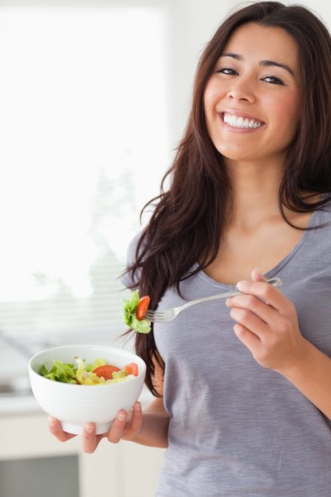 Pretty woman enjoying a bowl of salad while standing in the kitchen