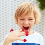 boy tasting ripe and fresh raspberries from his fingers
