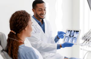 Black man dentist and woman patient looking at xray picture on digital tablet at clinic
