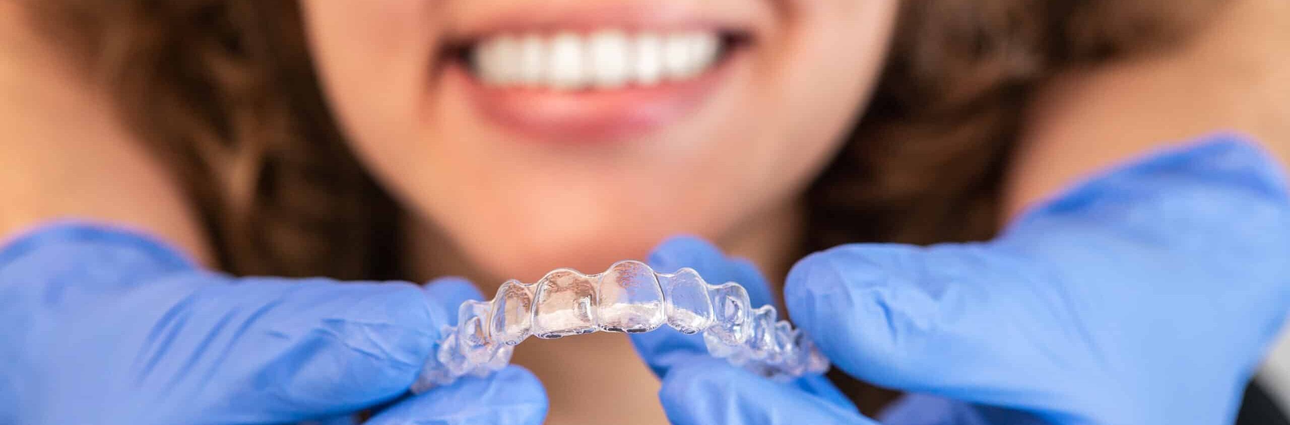 Orthodontist doctor putting silicone invisible transparent braces on woman teeth