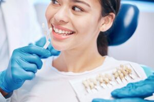 Female dentist showing patient a tooth shade guide to compare whitening, veneers, or crown options for a brighter smile